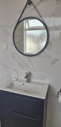Vanity unit with round mirror and marble-effect tiles by Misbourne Plumbing