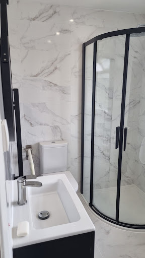 Marble shower room with black-framed curved enclosure by Misbourne Plumbing
